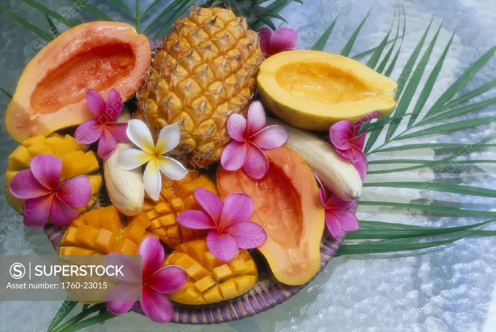Hawaii variety of fresh ripe cut fruit papaya mango banana whole pineapple display w/ plumeria flowers garnish
