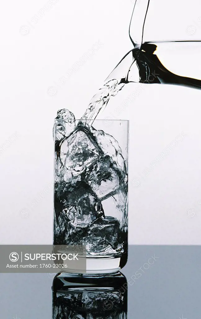 Water being poured from a pitcher into tall glass filled with ice cubes