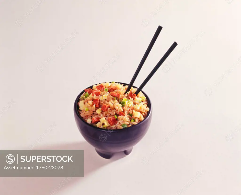 Studio shot of a bowl of fried rice with chopsticks sticking out of it.