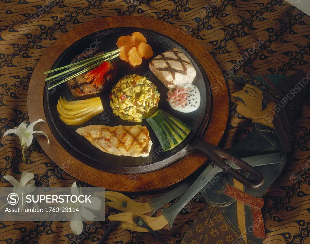 Indonesian fish, beef, and vegetables arranged on plate wooden puppet on table next to plate, tablecloth