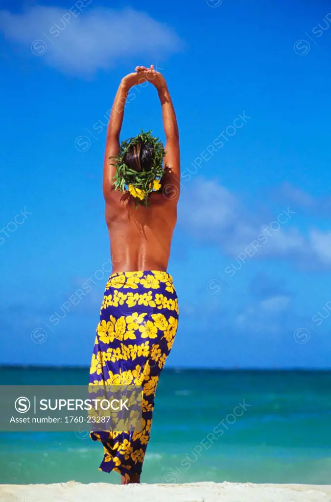Full length view of woman in long pareo, topless facing ocean, arms in air, blue sky
