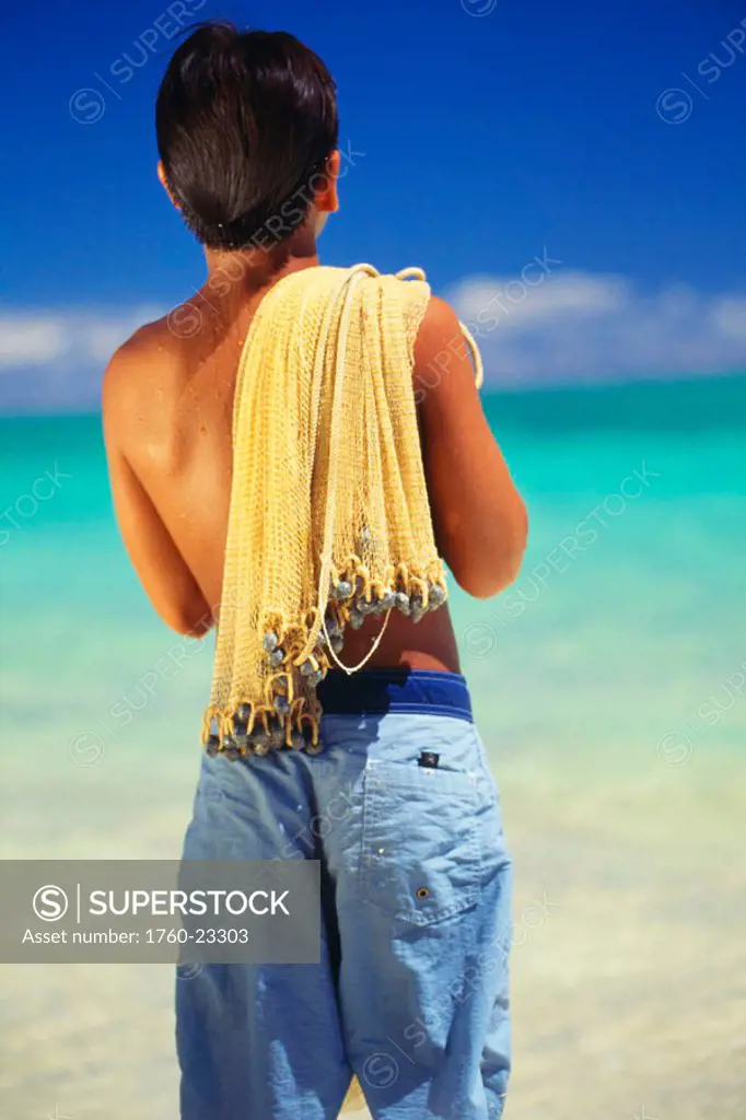 Young local boy with fishing net draped over shoulder, view from behind