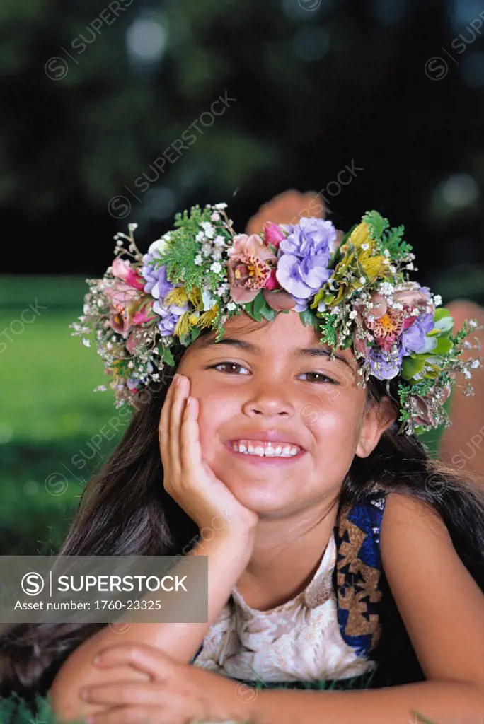 Closeup of little girl with flower haku, rests chin in palm, smiling, in park