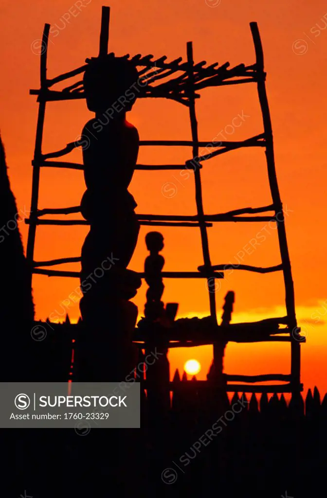 Hawaii, Big Island, Pu´uhonua O Honaunau National Historical Park, Structure and statues silhouetted by fiery sunset.