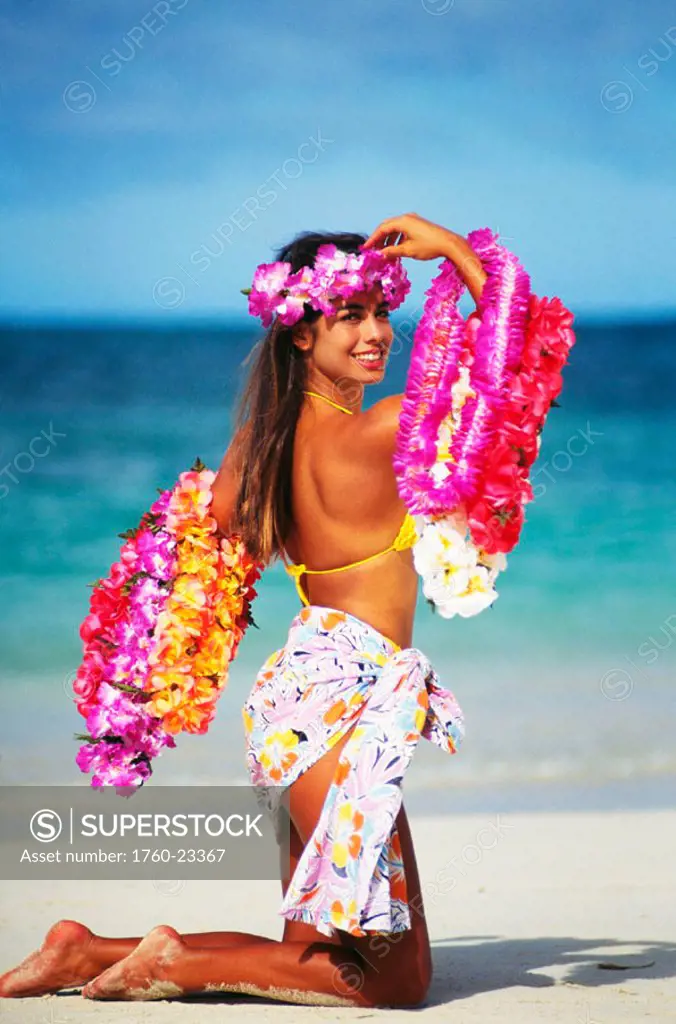 Hapa woman kneeling on beach holding leis.