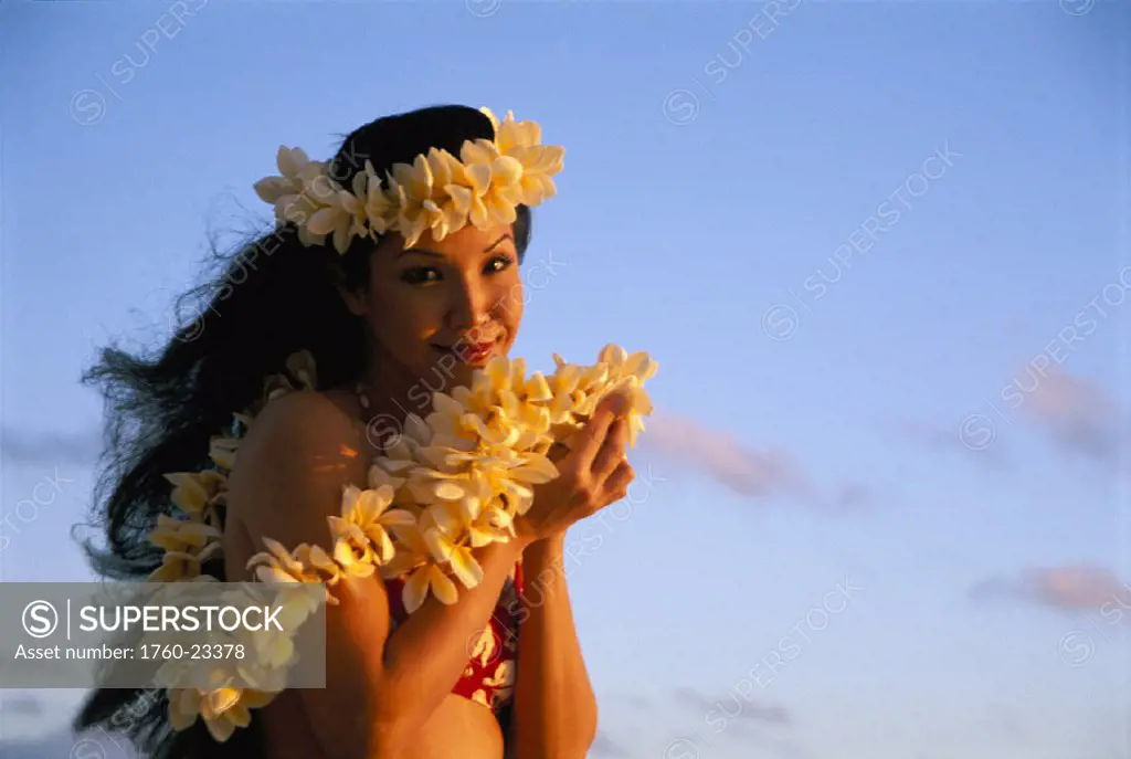 Closeup of young woman wearing plumeria haku and leis, soft blue sunrise sky