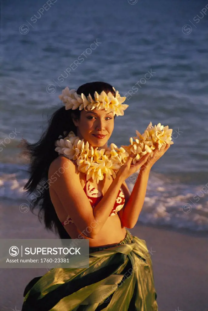 Front angle of woman on beach wearing plueria haku, holding plumeria lei, ocean background