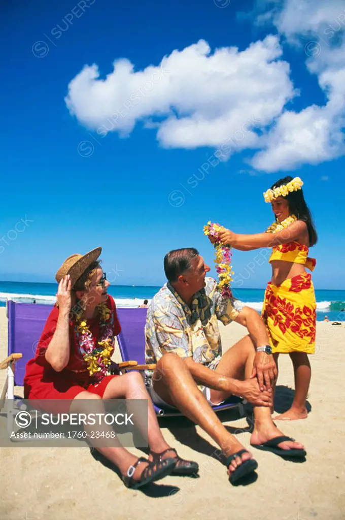 Senior Caucasian tourist couple getting lei from young girl on beach