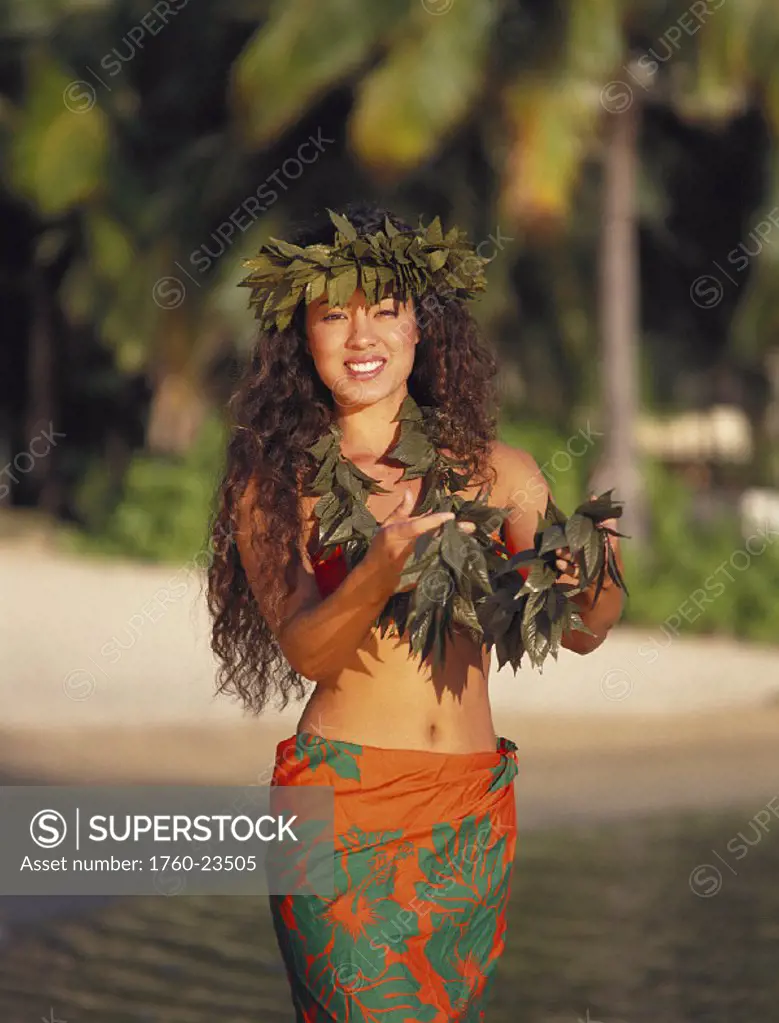 Local woman w/ haku on head, holds lei, smiling wears orange & green pareo