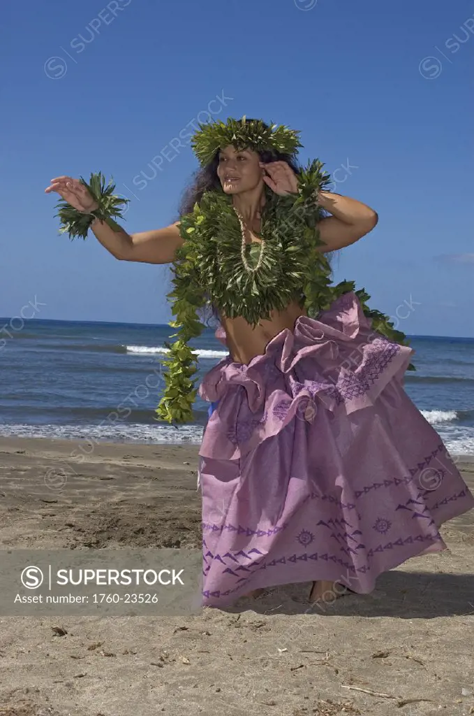 Hula dancer with haku lei in traditional outfit on shoreline, ocean background