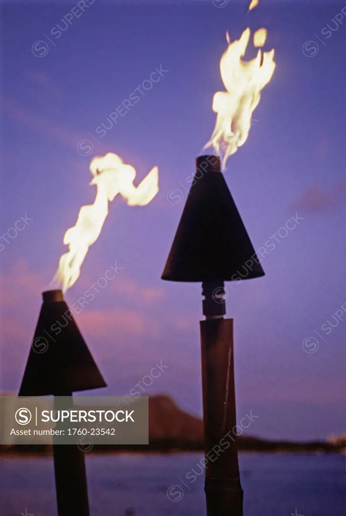 Hawaii, Oahu, Waikiki, Tiki torches burn at sunset with Diamond Head in background