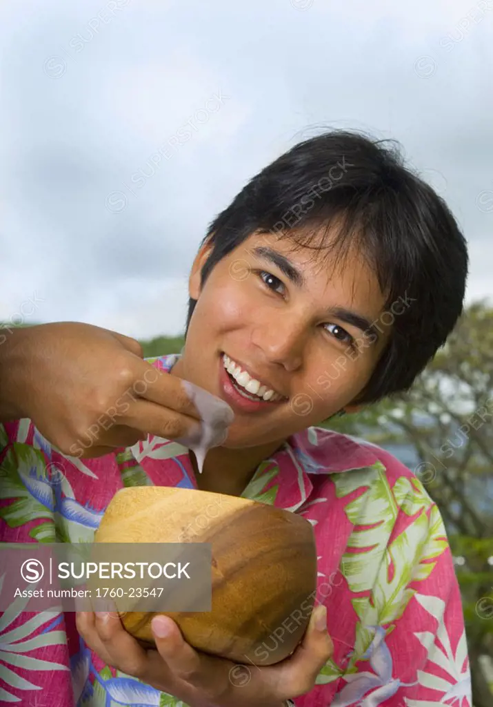 Hawaii, Young man eating poi with fingers out of wooden bowl.