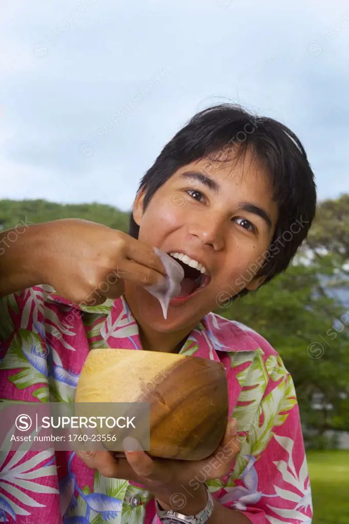 Young man eating poi with fingers out of wooden bowl.