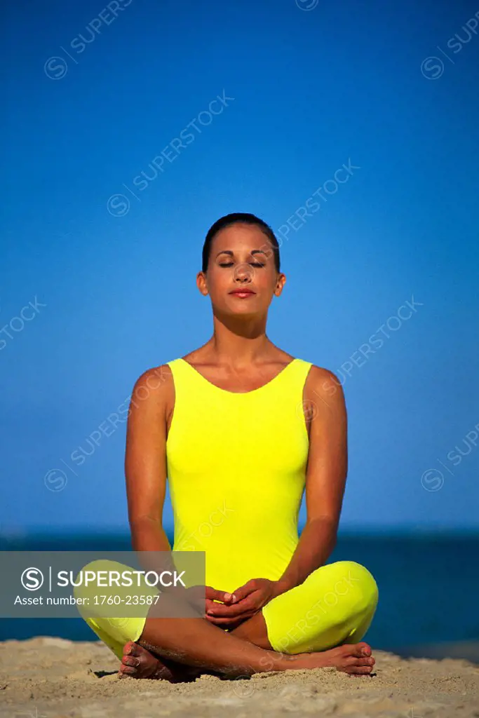 Woman in yellow bodysuit meditating on beach closeup w/ blue sky B1194