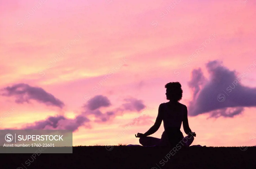 Woman doing Yoga on beach at sunset, silhouetted in pink purple skies