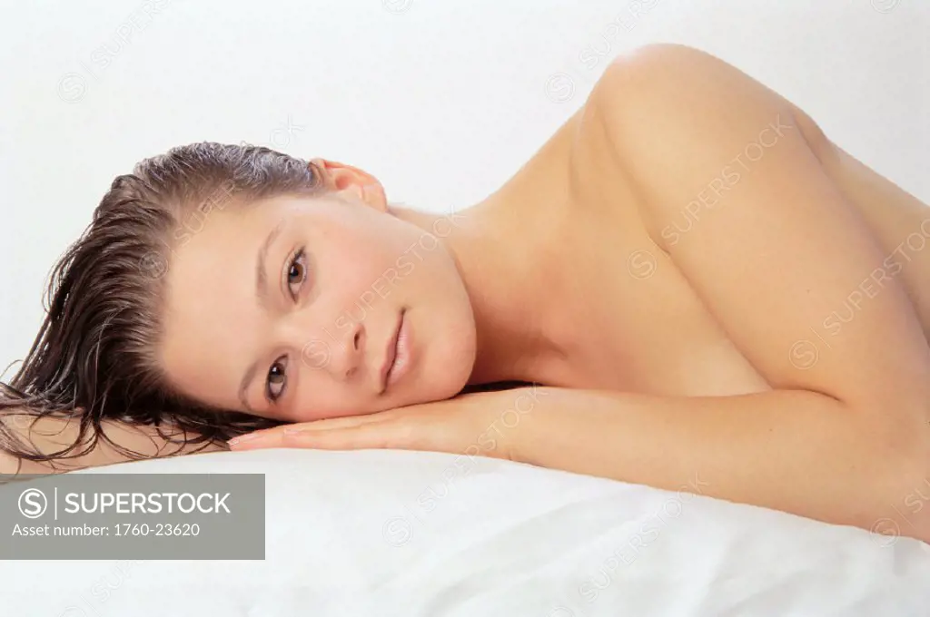 Studio shot of woman lying on pillow, relaxing, soft lighting, no clothing