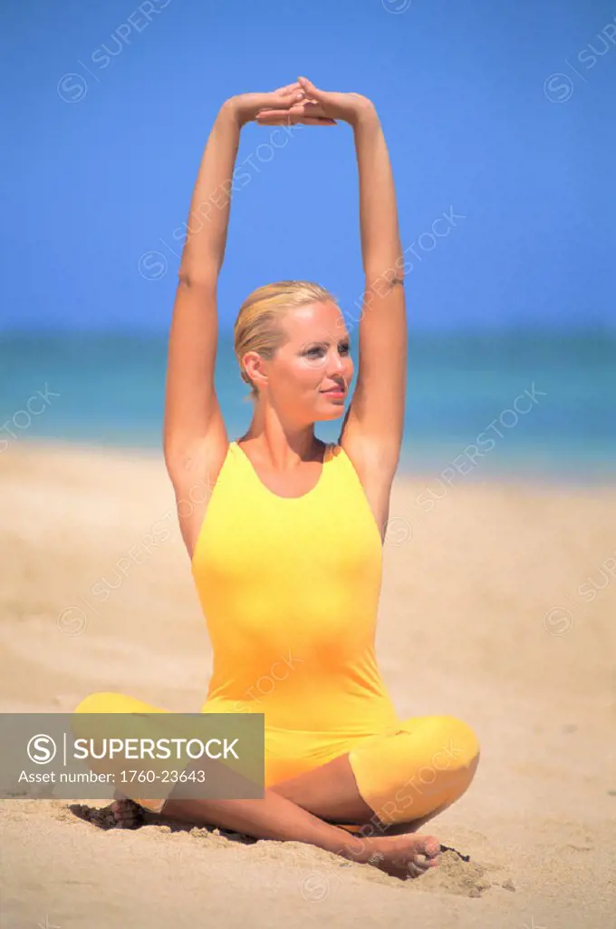 Blonde woman on beach sitting crosslegged in yellow leotard, stretching
