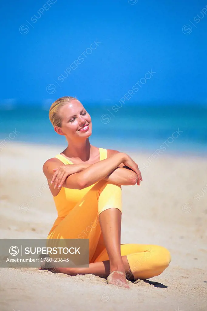 Young women sitting on beach in yellow leotard smiling, eyes closed C1219