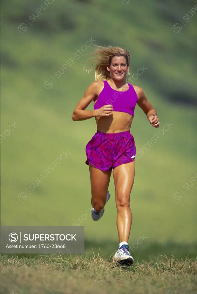 Front view blonde woman running on grass green blurry bkgd D1281 athletic in-shape Oahu