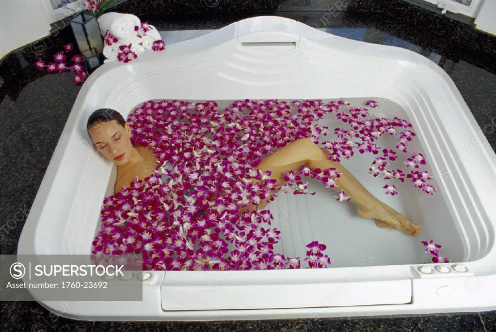 Woman lay white bath spa surrounded by vanda orchid flowers D1175 eyes closed relax