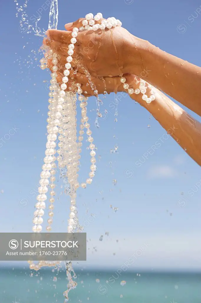 Close-up of hands holding strings of pearls, water pouring over them