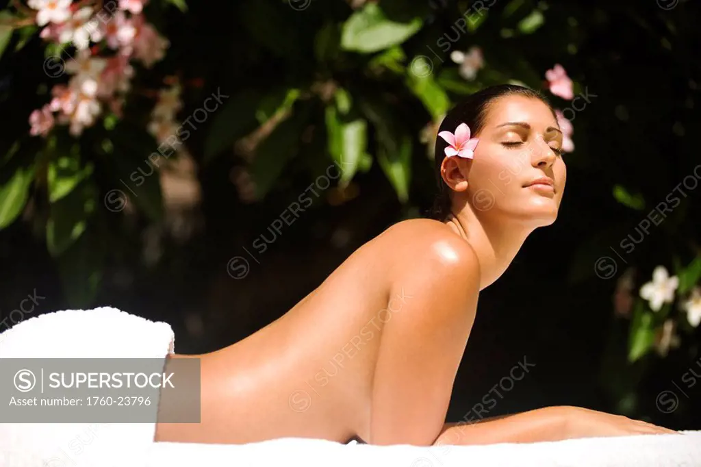 Hawaii, Topless girl laying down next to garden on massage table with pink plumeria in ear.