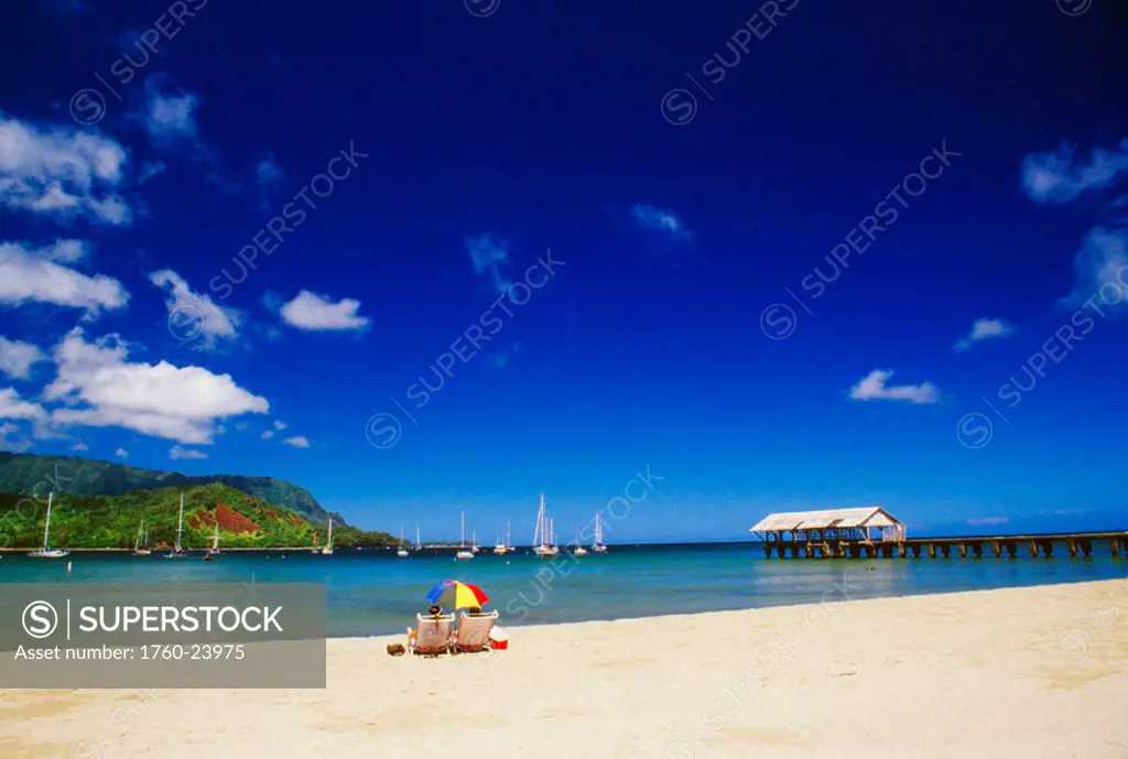 Hawaii, Kauai, Hanalei Bay, coastline with sailboats and dock, couple on the beach with umbrella
