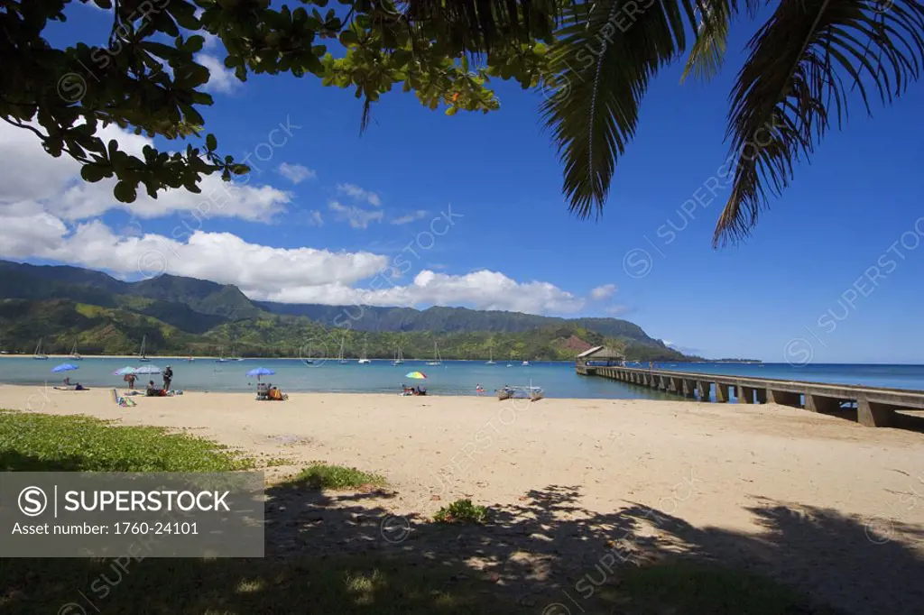 Hawaii, Kauai, Princeville, Hanalei Bay with pier walkway, tourists on beach, sailboats anchored in background