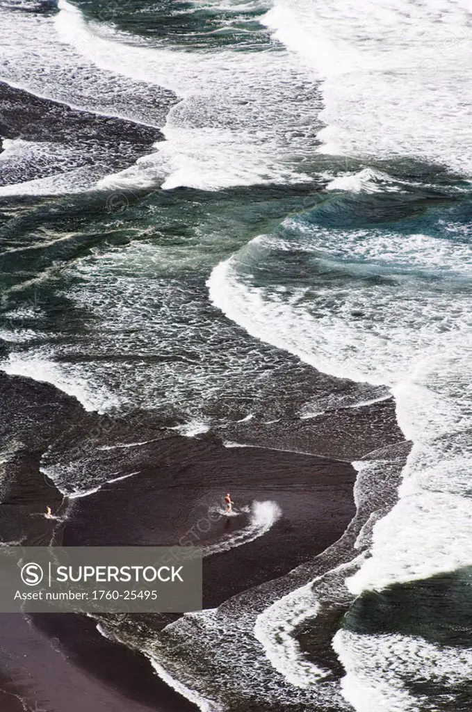 Hawaii, Big Island, Waipio Valley, Black sand beach, surfer walking out into pattern of rolling waves.