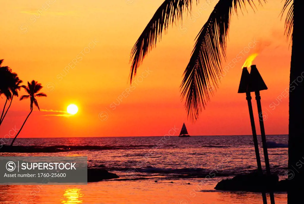 Hawaii, Big Island, Kohala, Waiulua Bay, Orange sunset with palm trees, sailboat and tiki torches.