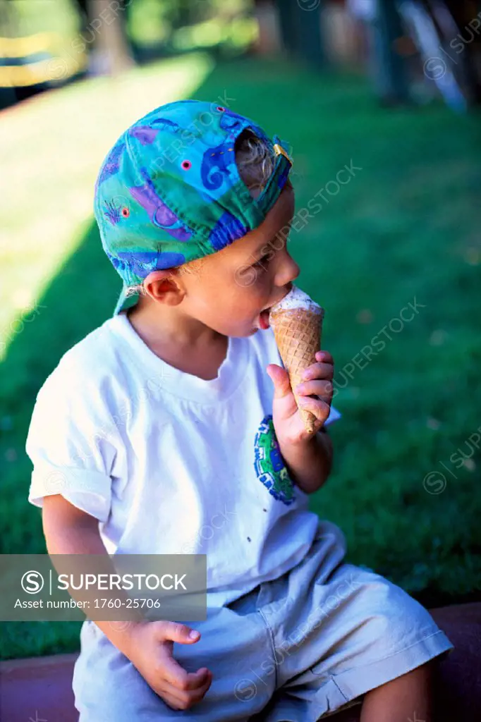 Young boy sits on bench eating ice cream cone B1095