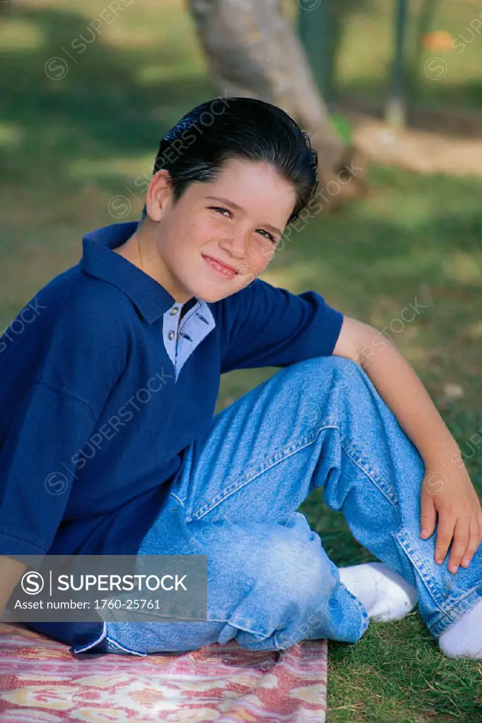 Smiling Caucasian boy sits in park, blurry background C1145