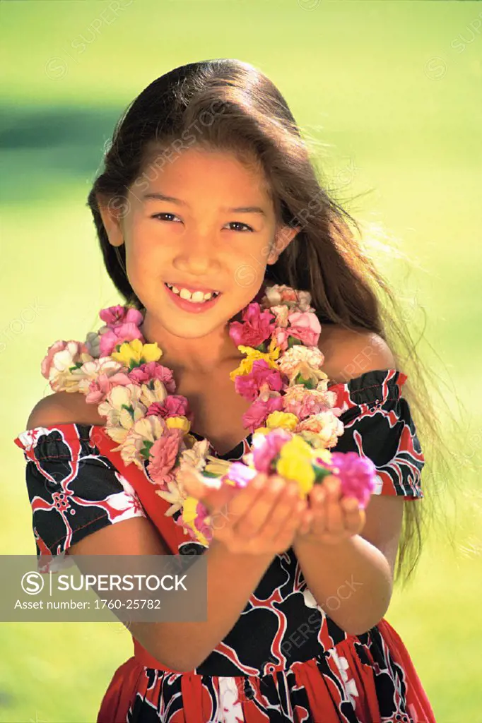Portrait shot of young local girl with leis in park, hold hands in front, smiling