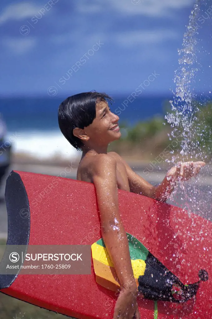 Side view of local boy with boogieboard under arm, fins at shower D1042