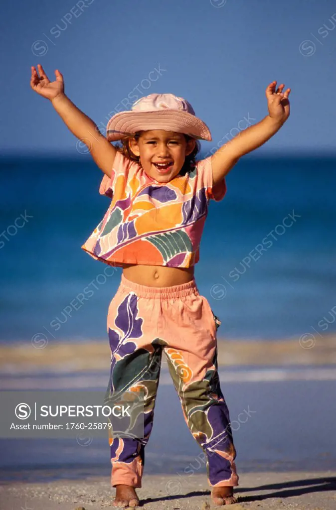 Little girl in colorful outfit and hat cheering on the beach