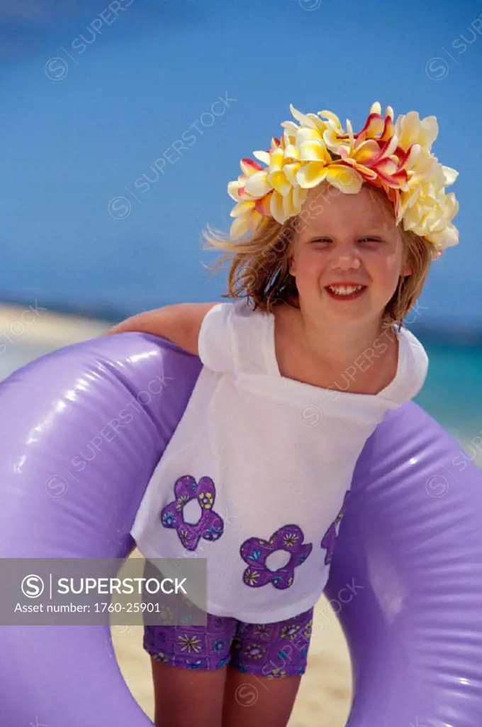 Smiling girl with plumeria haku holds purple inner tube behind back