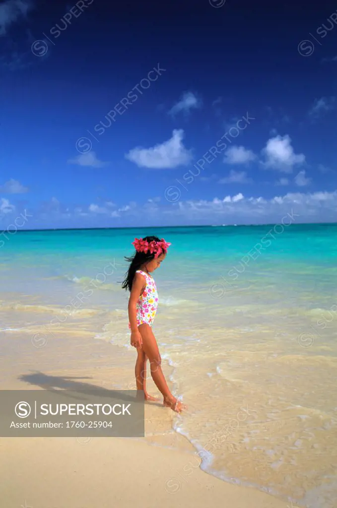 View of little girl walking on beach, pink haku, clear water, blue sky