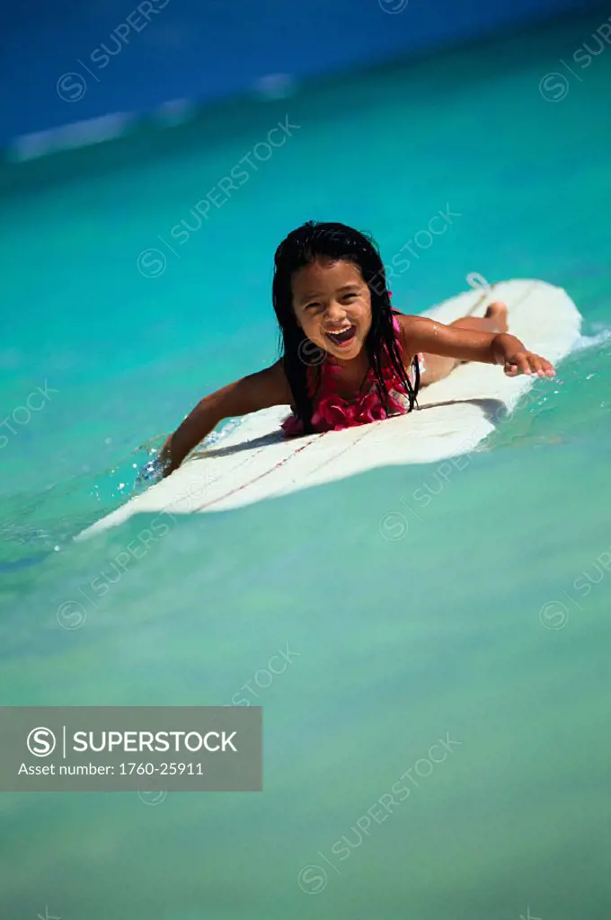 Front view of girl on surf board paddling in, smiling turquoise water