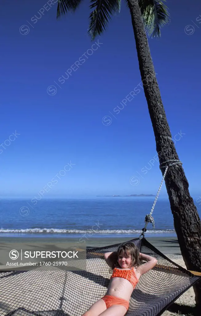 Fiji, Coral Coast, Smiling young girl relaxing in hammock on beautiful beach.
