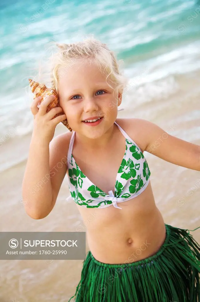 Hawaii, Oahu, Young girl in a hula skirt listening to a shell.