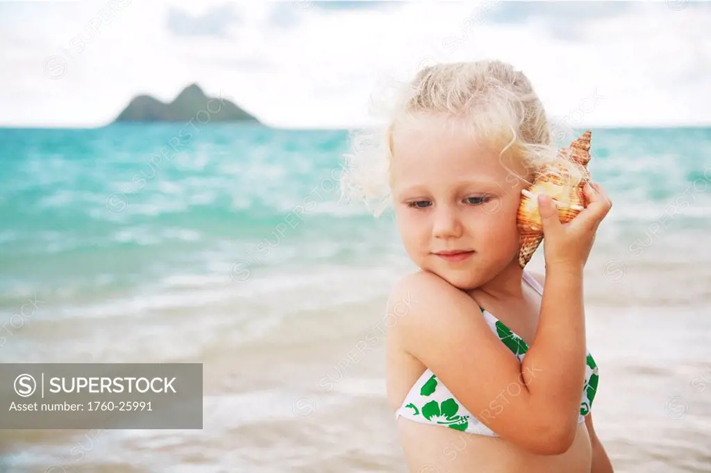 Hawaii, Oahu, Lanikai, Young girl listening to a shell.