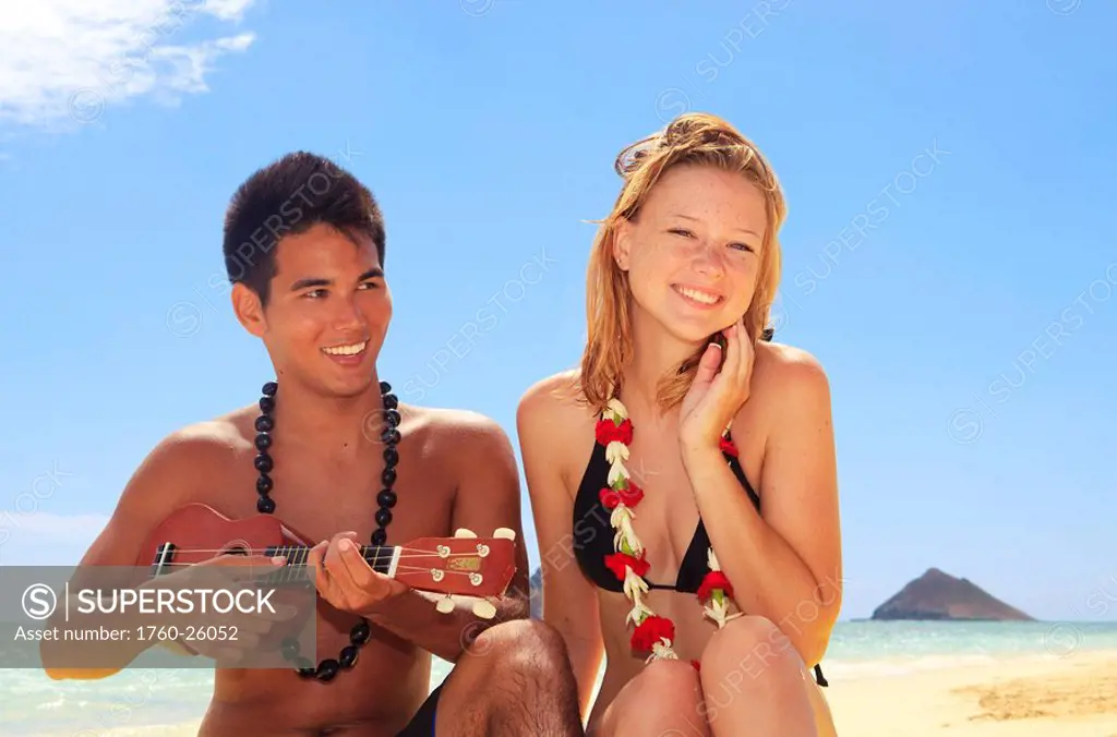 Hawaii, Oahu, Lanikai, Hawaiian beachboy plays his ukulele for a beautiful blond girl.