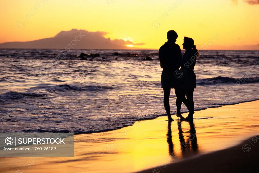 Romantic view of couple holding each other, shoreline at sunset