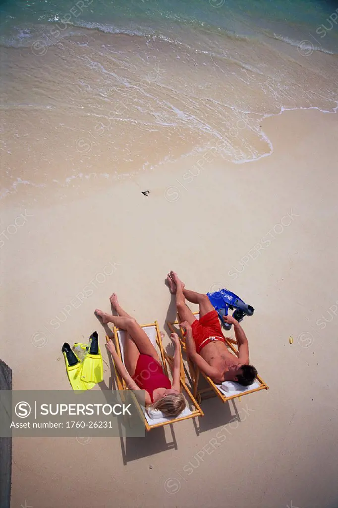 Vu fr above couple lounging along shoreline, beach chairs fins at side D1055