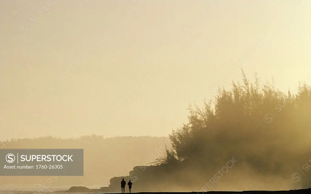 Hawaii, Kauai, Hanalei area, Couple walking along beach silhouetted against evening sky  NO MODEL RELEASE