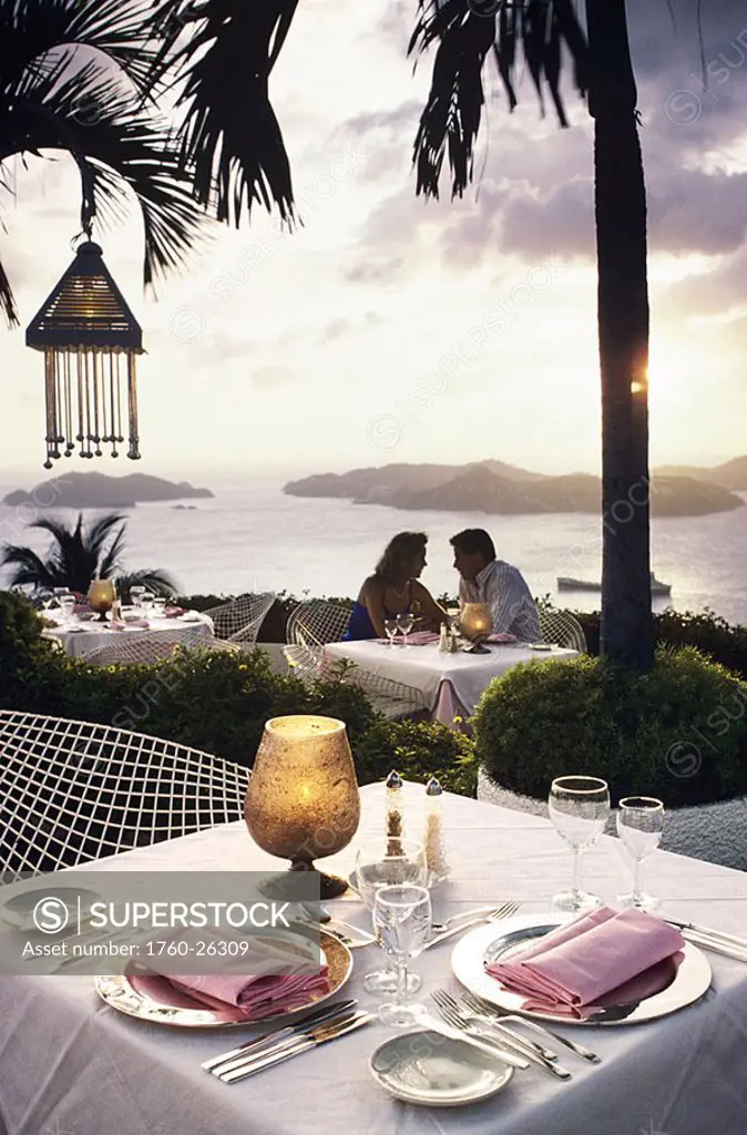 Mexico, Acapulco, Las Brisas hotel, Couple sitting at table overlooking ocean, Place setting detail on table
