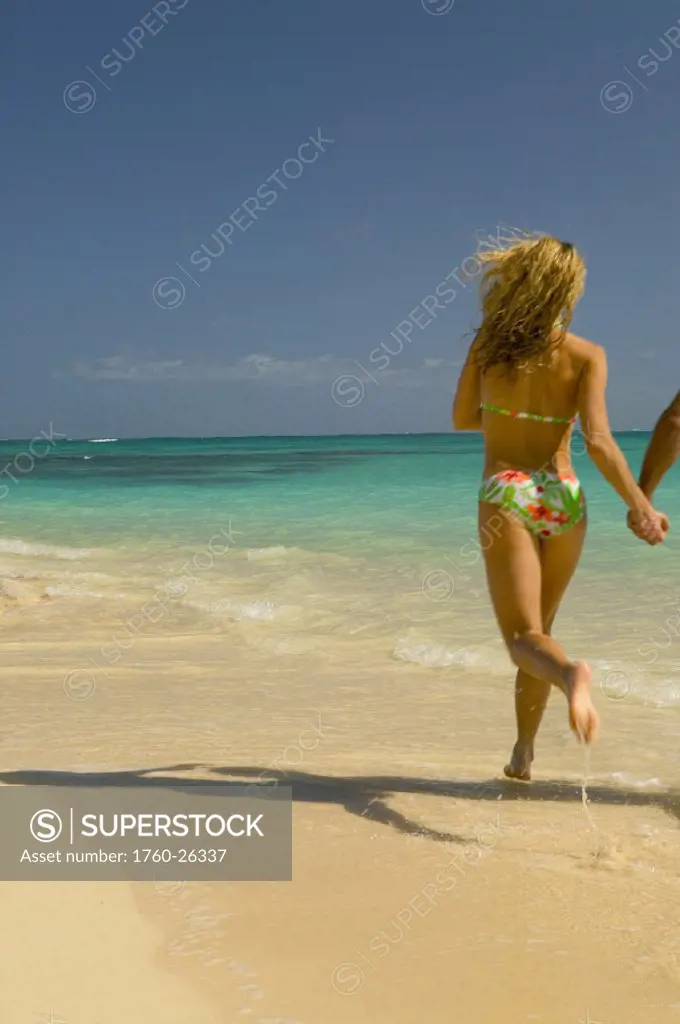 Hawaii, Oahu, Lanikai, Woman runs on the beach holding hands with man out of shot, new perspective.