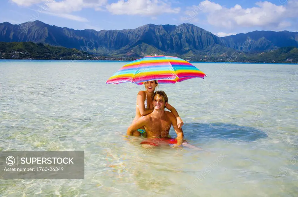 Hawaii, Oahu, Kaneohe, couple under a brightly colored umbrella in crystal clear water at the sandbar or ´dissapearing island´