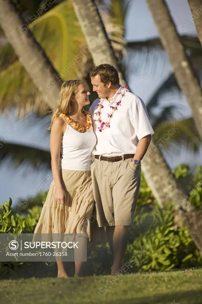 Hawaii, Maui, Honeymoon couple walks on grass under palm trees