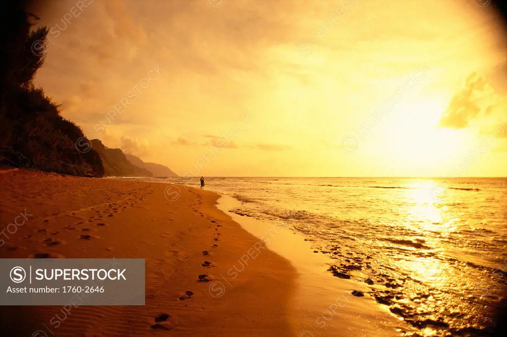 Hawaii Kauai, Haena Beach at sunrise, couple in distance footprints, golden sky A40D
